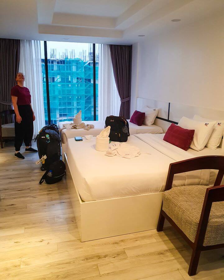 Krissie standing in the far left of the photo in a hotel room. There's two made up beds and a chair with suitcases and bags on the beds "Creating a Realistic Travel Budget: What You Need to Consider"