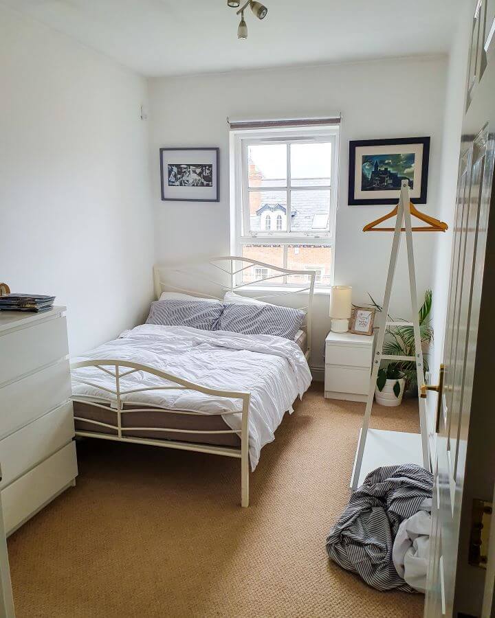 A small room with a double bed in the left corner, a bed side table, a clothes rack and a chest of drawers "Creating a Realistic Travel Budget: What You Need to Consider"