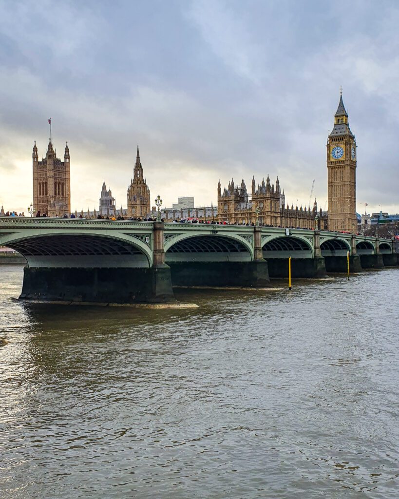 Westminster Bridge in London, England which is a green bridge with 6 arches for the Thames river to go under. On the other side is Big Ben and The Houses of Parliament which are gold buildings with lots of towers and points "How to Have the Best Time in London (For Free!)"