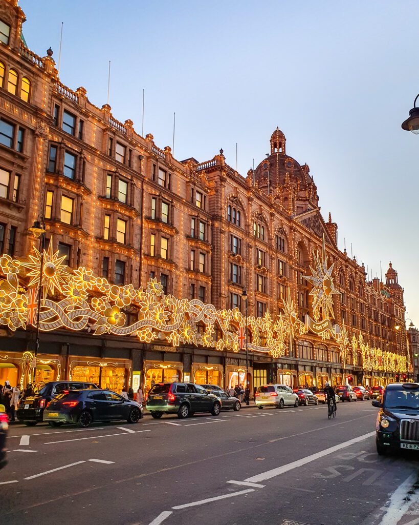 A huge grand building that runs along one entire road in London, England. The building has beautiful Christmas decorations on it in with white and yellow lights lit up in the pre sunset light "How to Have the Best Time in London (For Free!)"