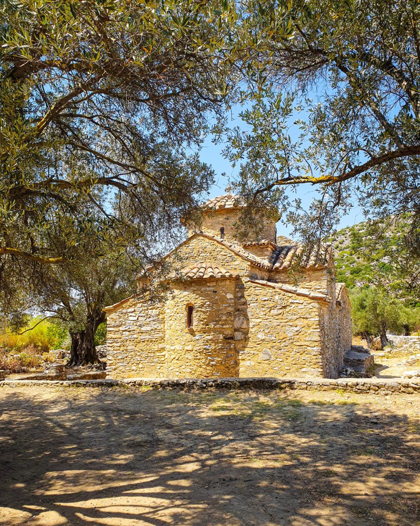 Empty dirt ground in front of a little stone church with tiled roofs surrounded by trees just outside Halki in Greece "How to Have the Best Time in Naxos on a Budget"