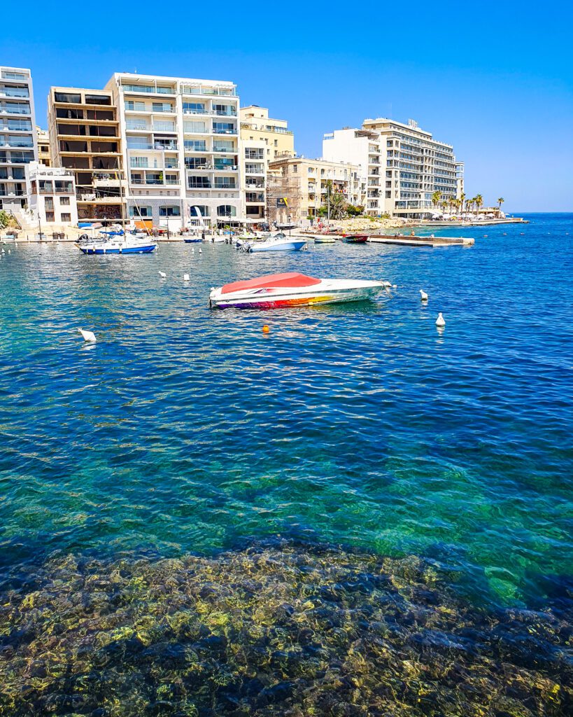 A view of some white buildings across some crystal blue water with some boats in between in Malta "Where Are the Best Areas to Stay in Malta?"