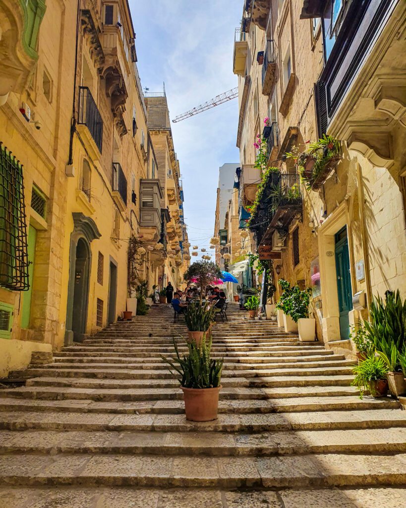  A beautiful street in Valletta, Malta with old sandstone coloured buildings and lots of plants "Where Are the Best Areas to Stay in Malta?"