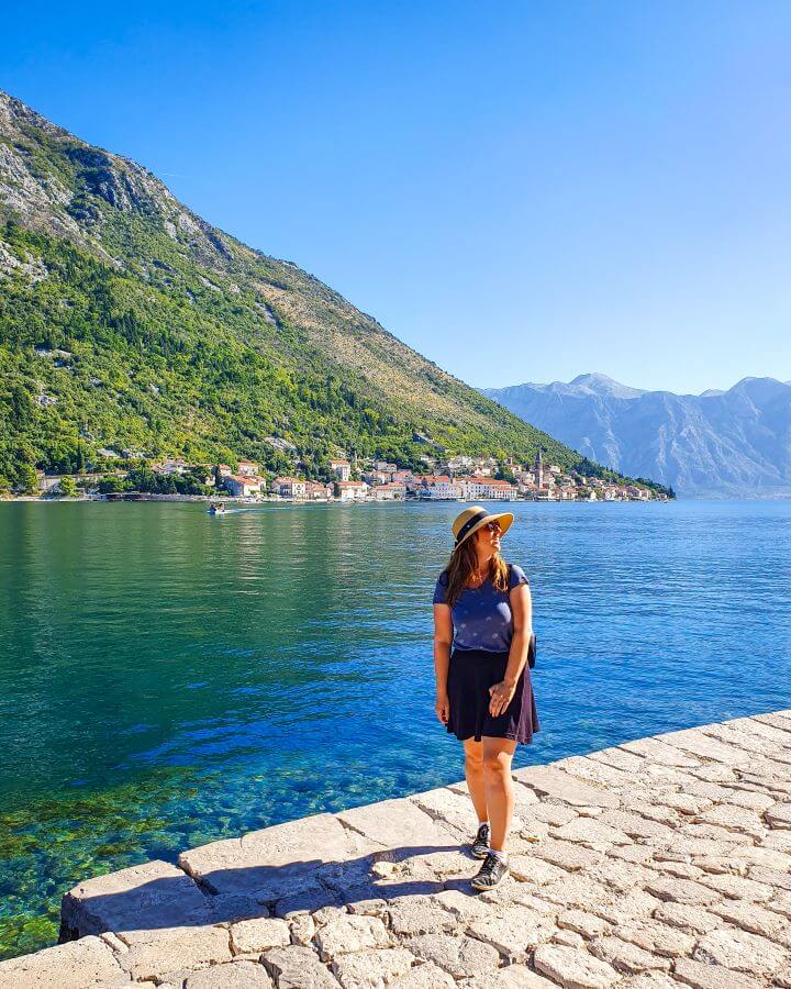 Katherine standing on a cobbled path with Kotor Bay, Montenegro behind her. There is a large stretch of water with big hills behind it and some little towns along the edge of the water "Navigating the Schengen Area: What You Need To Know (Free Tracker Included)"