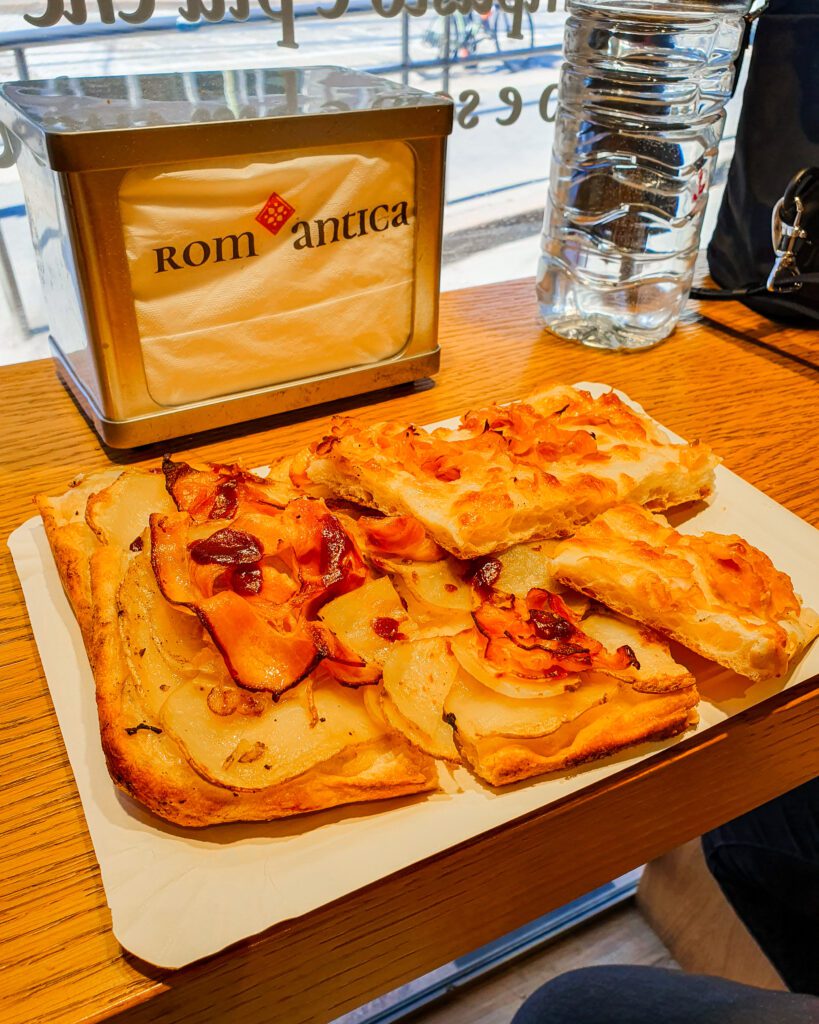 A plate of square slices of pizza with a bottle of water and some napkins that say "Romantica" on them which is an amazing pizza place is Milan, Italy "How to Spend Your Time in Verona on a Budget"