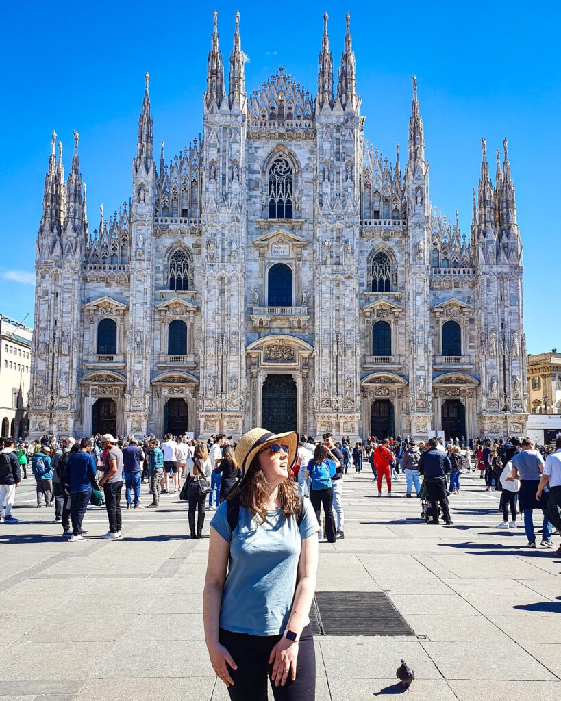 Krissie smiling and standing in front of the Duomo in Milan, Italy. The Duomo is a huge church with 10 large spires and is made of white and grey marble "How to Spend Your Time in Verona on a Budget"