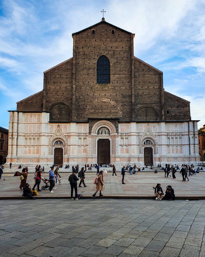 A huge basilica in Bologna, Italy with people walking in the town square in front of it. The top half of the Basilica is brown, and the bottom is white "How to Spend Your Time in Verona on a Budget"