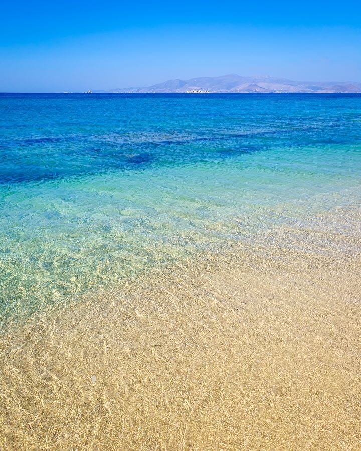 The clearest water we've ever seen, which has a gradient from lighter water to a dark blue further out. On the edge of the water you can see another Greek island "How to Have the Best Time in Naxos on a Budget"