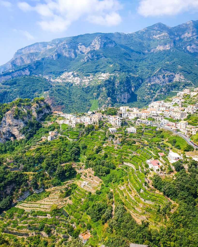 A sprawling view over the hills of the Amalfi Coast, Italy. There are green hills, white buildings and big green cliffs "See Naples On a Budget With These Six Great Ideas!"