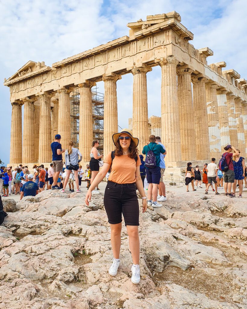 Krissie smiling and standing in front of the Parthenon with lots of people behind her in Athens, Greece "How to Make the Most of the Athens Combined Ticket"