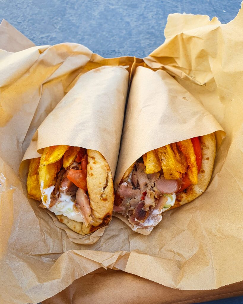 A picture of two gyros in Athens, Greece wrapped in brown paper. The gyros have tomatoes, hot chips, meat and garlic sauce in them and they are delicious! "The 6+ Best Budget Friendly Activities in Athens"