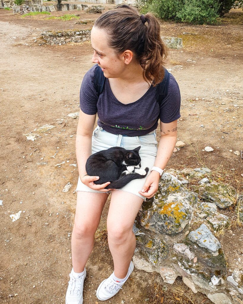 Krissie sitting on a rock with a little black and white cat curled in her lap in Athens, Greece "The 6+ Best Budget Friendly Activities in Athens"