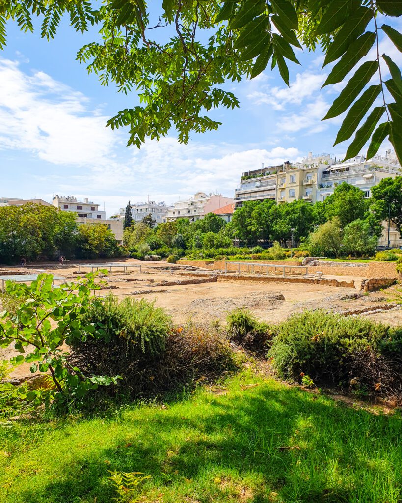 A view of some stone ruins of Aristotle's Lyceum with buildings behind it and trees and grass in the foreground in Athens, Greece "How to Make the Most of the Athens Combined Ticket"