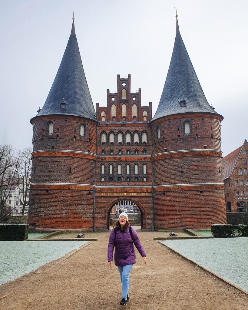 Krissie smiling and standing in front of the gothic looking Holsten gate in Lübeck, Germany "How to See Lübeck in a Day Trip from Hamburg"