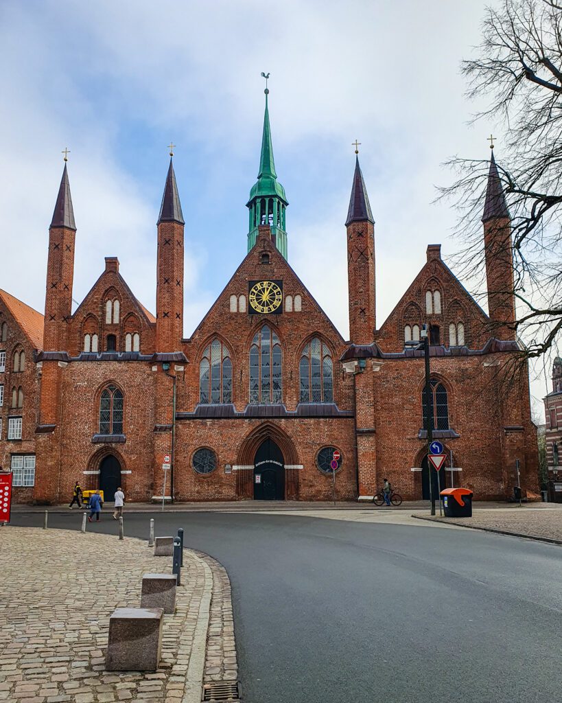 The Hospital of the Holy Spirit in Lübeck, Germany with its four red brick spires and one bigger green spire in the middle "How to See Lübeck in a Day Trip from Hamburg"