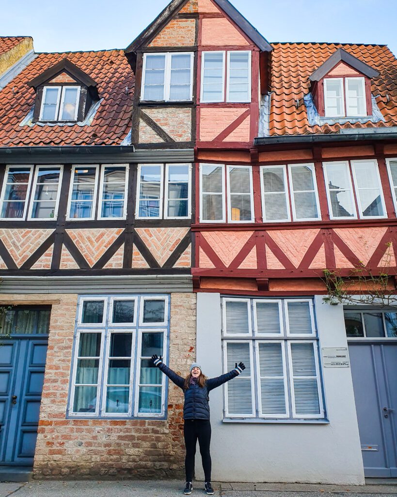 Katherine putting her hands up in excitement in front of two old looking European buildings in Lübeck, Germany "How to See Lübeck in a Day Trip from Hamburg"