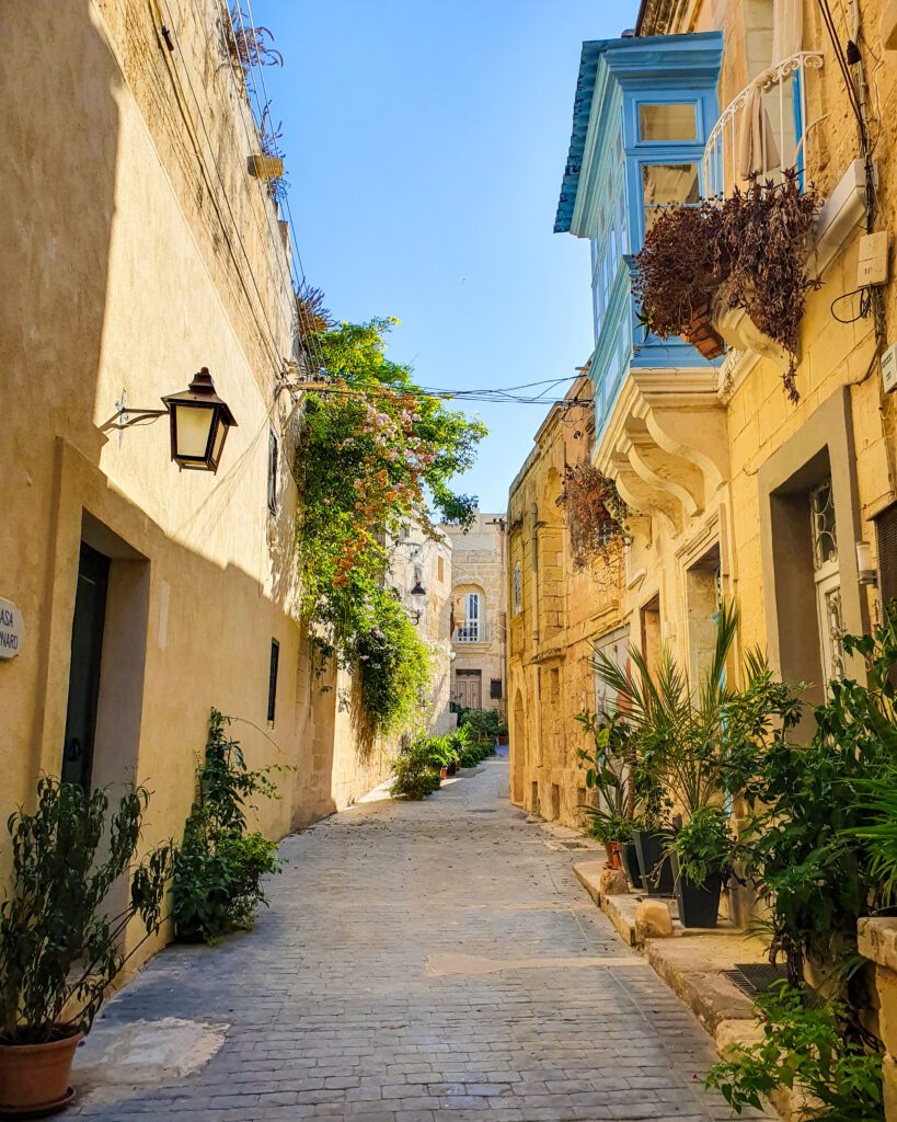 A beautiful street in Rabat, Malta with sandstone coloured buildings and lots of plants "Eight Amazing Things to See in Malta"