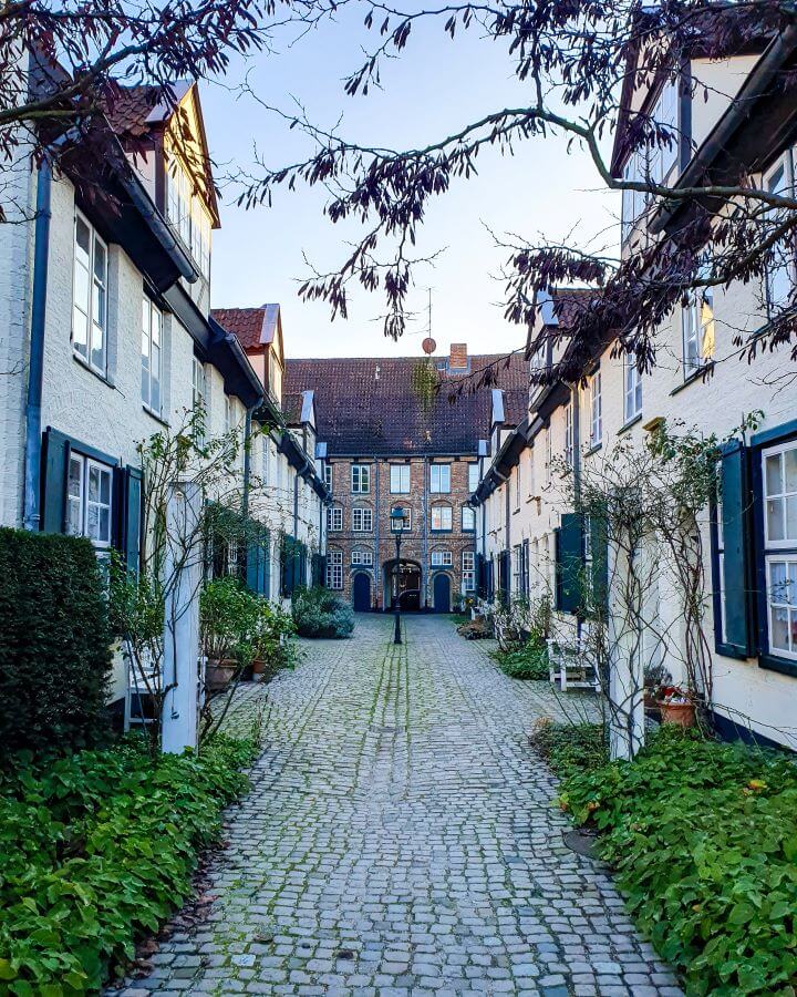 The Glandorps Hof courtyard in Lübeck, Germany. The courtyard is small and has old buildings and a cobbled street with a light post in the middle "How to See Hamburg on a Budget"