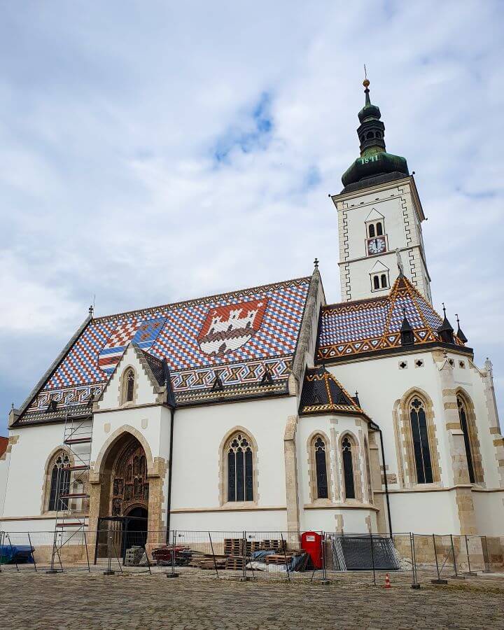 St Mark's Cathedral which is a small church in Zagreb, Croatia with an amazing tiled roof that has a mosaic of two coats of arms, one of the city of Zagreb and the other of the Triune Kingdom of Croatia, Slavonia and Dalmatia "How to Affordably See Zagreb"