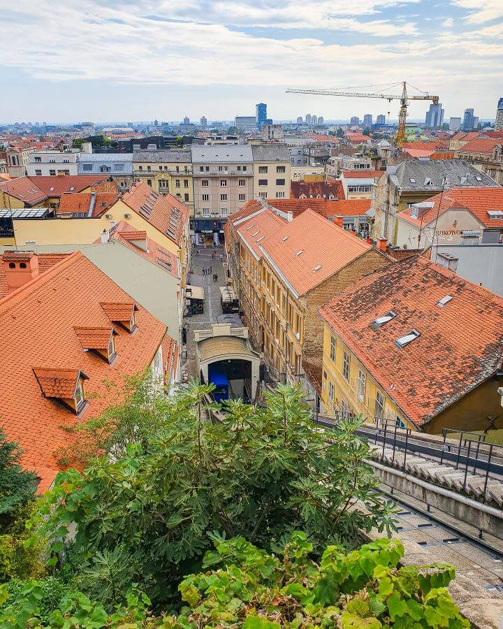 A view of the Zagreb funicular in Croatia and behind it is a view over Zagreb with it's orange roofs "How to Affordably See Zagreb"