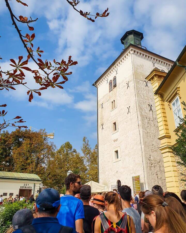 The Lotrščak tower in Zagreb, Croatia with lots of people waiting underneath "How to Affordably See Zagreb"