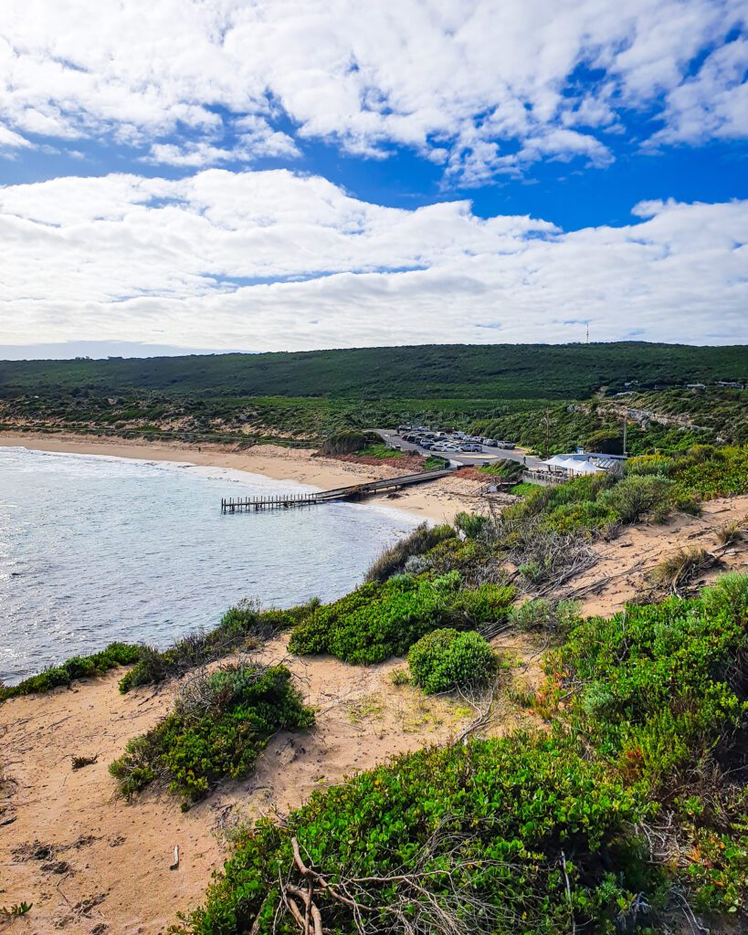 A view taken from a hill down to a beach in Margaret River, WA. There's a wooden jetty on the beach and lots of green bushes and yellow sand around "How to See Perth in a Weekend"