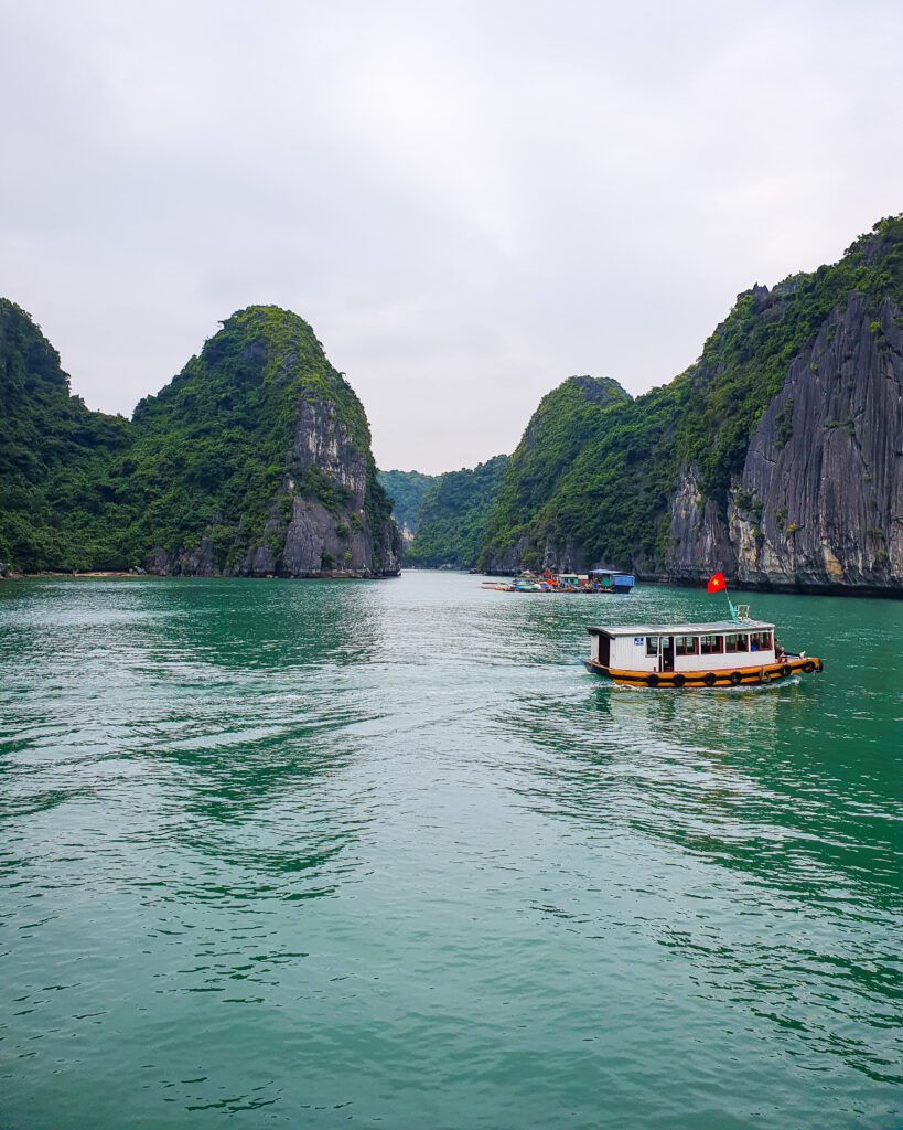 In Lan Ha Bay, Vietnam, with its blue green water and limestone hills with green bushes all over them. There's also a couple of little boats, one with the Vietnamese flag on top "Lan Ha Bay: A Beautiful Alternative to Halong Bay"