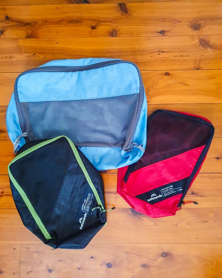 Three packing cubes lying on the ground, one blue bigger one, and 2 smaller red and green ones "The Ultimate Travel Packing Guide: 39 Essentials for Every Trip"