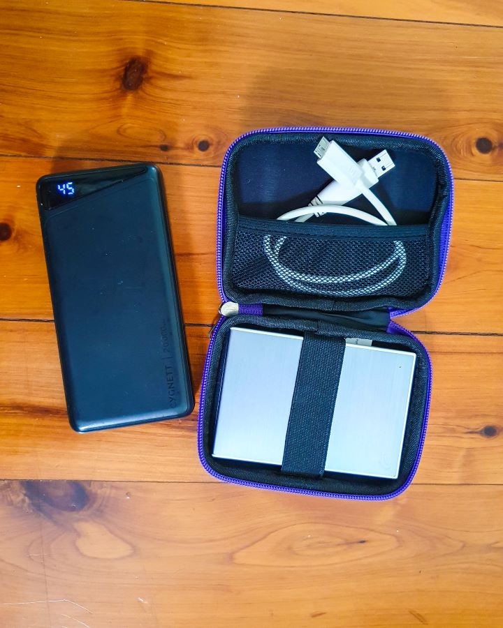 Our black Cygnett 20000mAh portable charger lying on the floor next to a purple hard drive case with a silver hard drive inside and a white charging cable in it too "The Ultimate Travel Packing Guide: 39 Essentials for Every Trip"