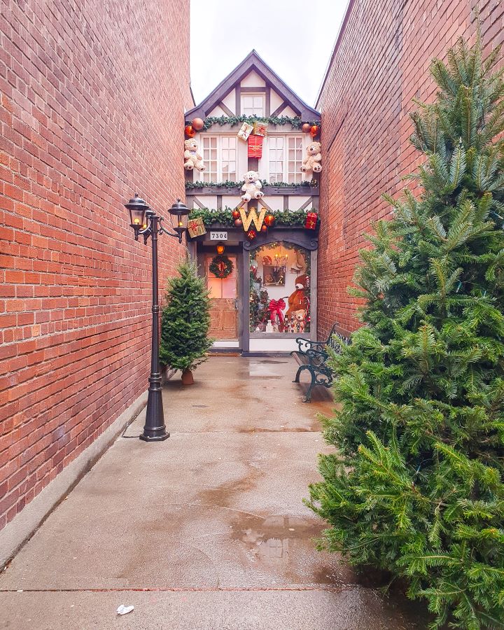 A little alleyway off Wellington street in Montréal, Canada. The alley has tall brick walls on both side with the cutest little house at the end. It looks like an old English building with wooden beams and white in between. It's decorated for Christmas with a wreath on the front and teddy bears. There's also a Christmas tree on the left and one closer to the camera on the right too "Eight Great Free Things To See In Montréal"