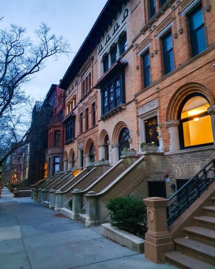 A street in Park Slope New York City, USA. The street is lined with three story brownstone buildings with stairs leading up to them. On the left is a path with bare trees on it too "Non-Touristy Activities for Return Visitors to New York City"