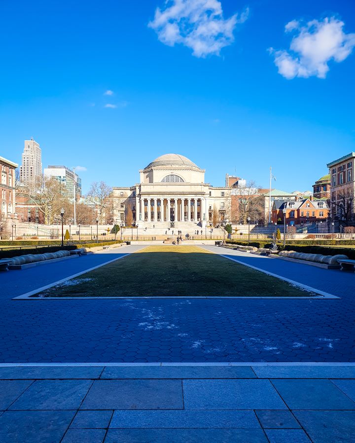 A large shadowed area on the Columbia University campus in New York City, USA. There's a big grass area with a path around it and behind that is a large stone building with a big dome on top. Around it are more buildings and above is the blue sky "Non-Touristy Activities for Return Visitors to New York City"