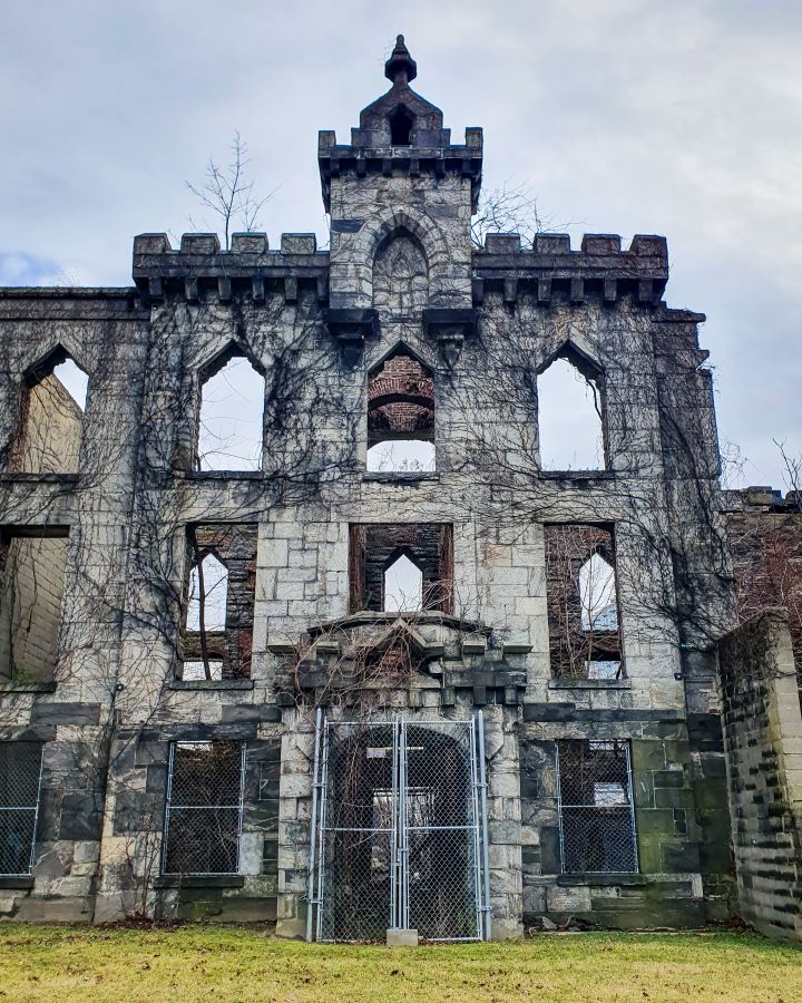 The Gothic façade of the old smallpox hospital on Roosevelt Island in New York City, USA. It's just the front and the inside is empty and you can see other walls of the building through the empty windows. The brick façade is three levels high with windows, a little tower at the top and the whole thing is covered in ivy "Non-Touristy Activities for Return Visitors to New York City"